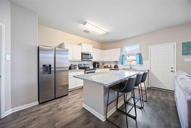 kitchen featuring stainless steel appliances, dark wood-type flooring, white cabinets, a kitchen island, and a breakfast bar area