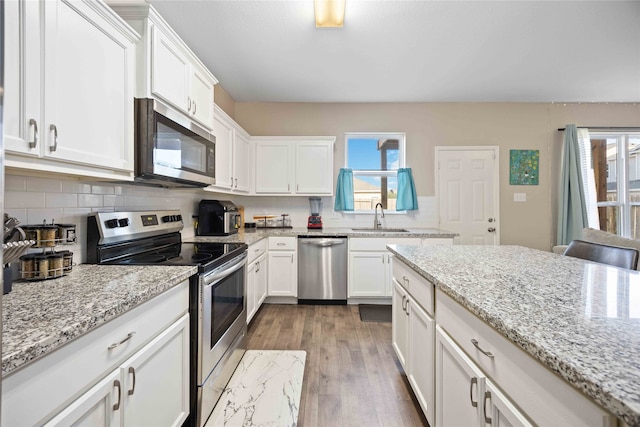 kitchen featuring sink, stainless steel appliances, tasteful backsplash, light stone counters, and white cabinets