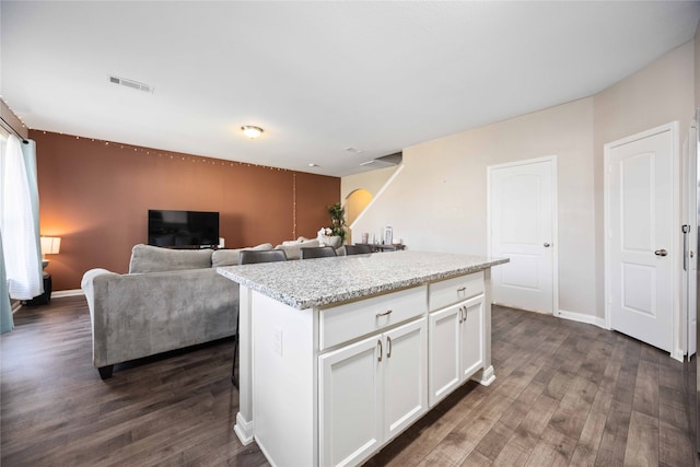 kitchen with dark hardwood / wood-style floors, white cabinetry, a kitchen island, and light stone counters