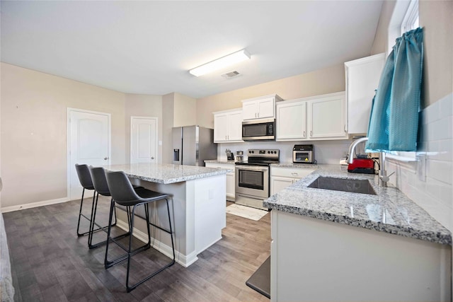 kitchen with a kitchen breakfast bar, sink, a kitchen island, white cabinetry, and stainless steel appliances