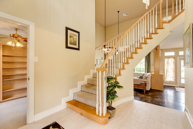 staircase with tile patterned flooring, a high ceiling, and ceiling fan with notable chandelier