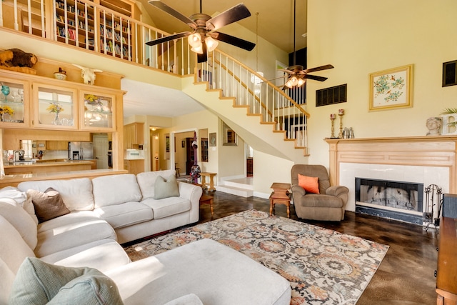 living room with ceiling fan, a tile fireplace, and a high ceiling