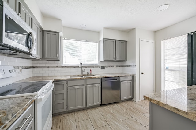 kitchen featuring light stone countertops, stainless steel appliances, sink, and gray cabinetry