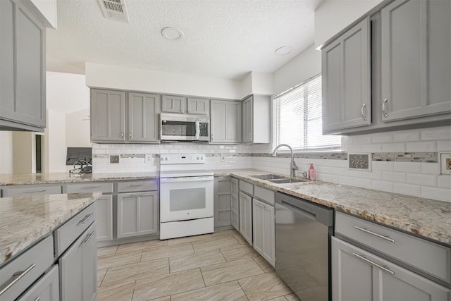 kitchen with gray cabinetry, stainless steel appliances, sink, light stone countertops, and tasteful backsplash