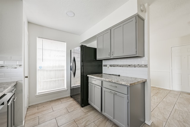 kitchen with black refrigerator with ice dispenser, light stone counters, plenty of natural light, and gray cabinetry