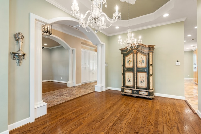 interior space featuring hardwood / wood-style floors, decorative columns, an inviting chandelier, and ornamental molding