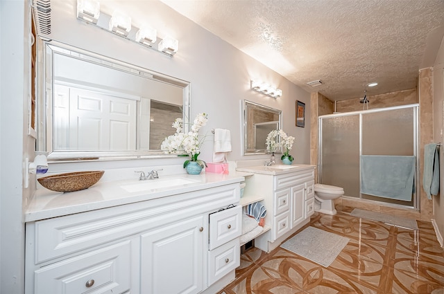 bathroom featuring vanity, toilet, a shower with shower door, and a textured ceiling