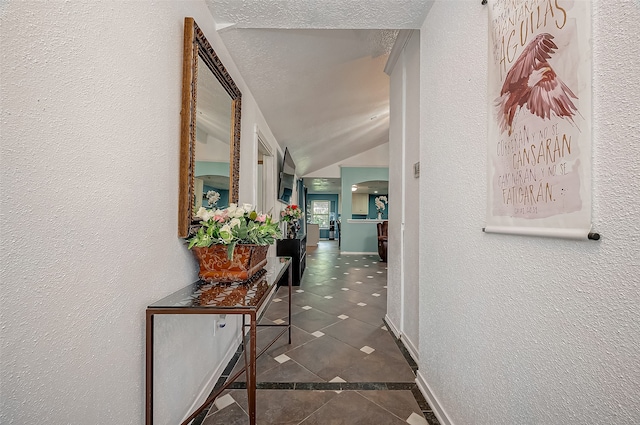 corridor featuring vaulted ceiling, a textured ceiling, and dark tile patterned floors