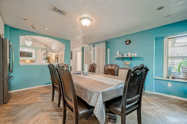 dining space featuring light parquet flooring, lofted ceiling, and a textured ceiling