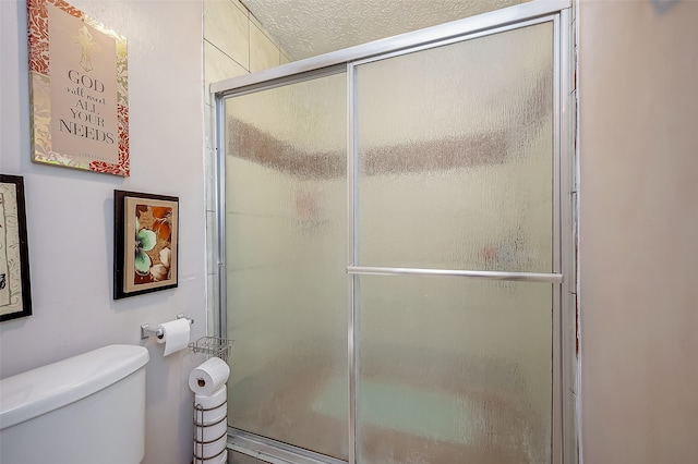 bathroom with a textured ceiling, a shower with shower door, and toilet