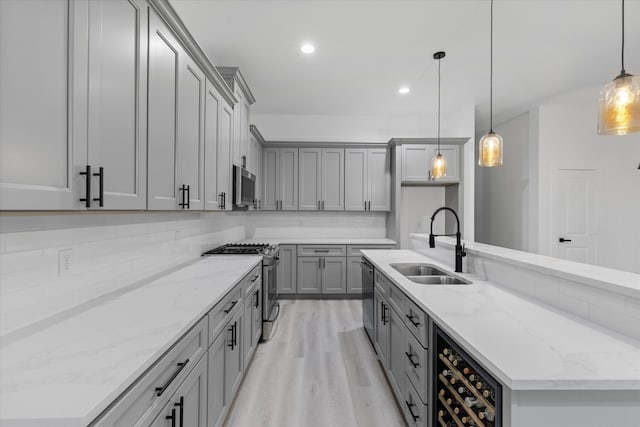 kitchen featuring appliances with stainless steel finishes, light wood-type flooring, beverage cooler, decorative light fixtures, and sink