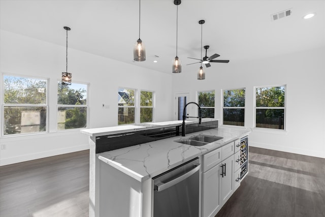 kitchen featuring light stone counters, dishwasher, a kitchen island with sink, and sink