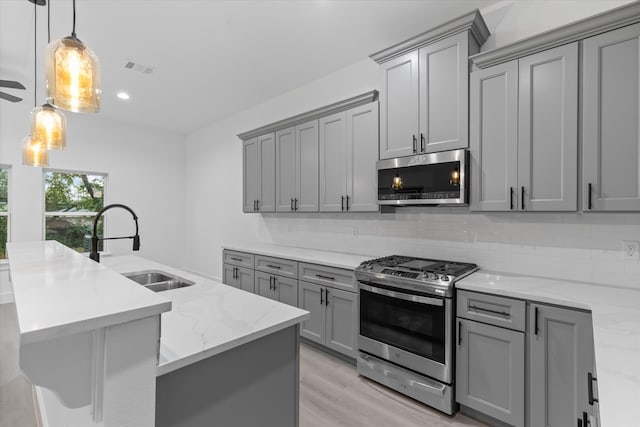 kitchen with pendant lighting, gray cabinets, light stone counters, sink, and appliances with stainless steel finishes