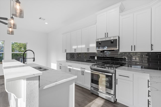 kitchen with light stone countertops, stainless steel appliances, white cabinetry, and hanging light fixtures