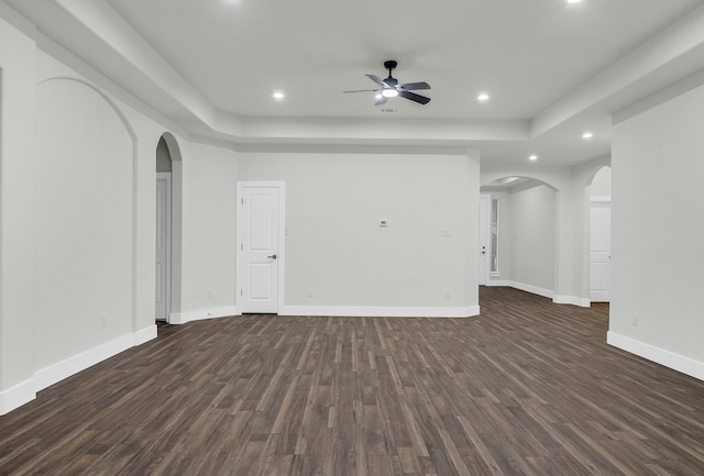 unfurnished room with dark wood-type flooring, a raised ceiling, and ceiling fan