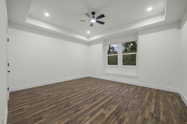 empty room featuring dark wood-type flooring, ceiling fan, and a raised ceiling