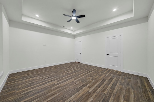 spare room with dark wood-type flooring, a raised ceiling, and ceiling fan