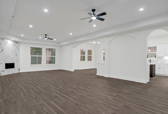 unfurnished living room with dark wood-type flooring, ceiling fan, a tray ceiling, and a fireplace