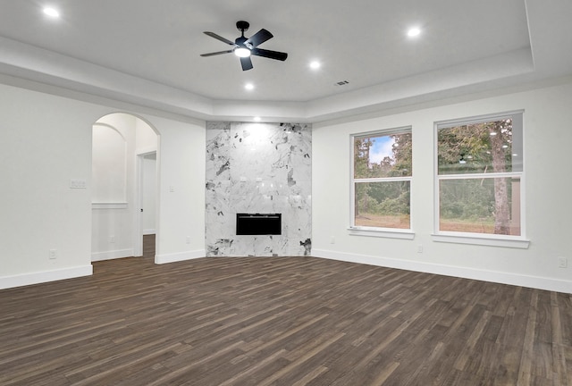 unfurnished living room with a high end fireplace, a raised ceiling, dark hardwood / wood-style flooring, and ceiling fan