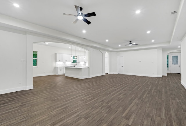 unfurnished living room with a tray ceiling, dark wood-type flooring, and ceiling fan