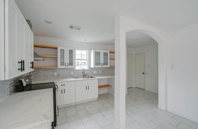 kitchen with stainless steel range with electric stovetop, sink, decorative backsplash, white cabinets, and wall chimney range hood