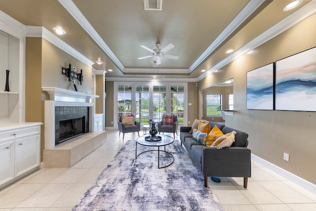 tiled living room featuring ceiling fan, a tiled fireplace, a raised ceiling, and crown molding