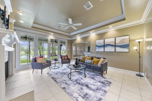 living room with ceiling fan, ornamental molding, a tray ceiling, and light tile patterned flooring