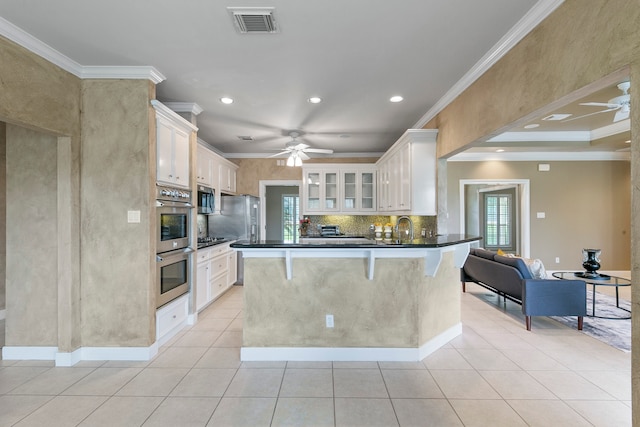 kitchen featuring white cabinets, stainless steel appliances, a kitchen breakfast bar, ceiling fan, and ornamental molding