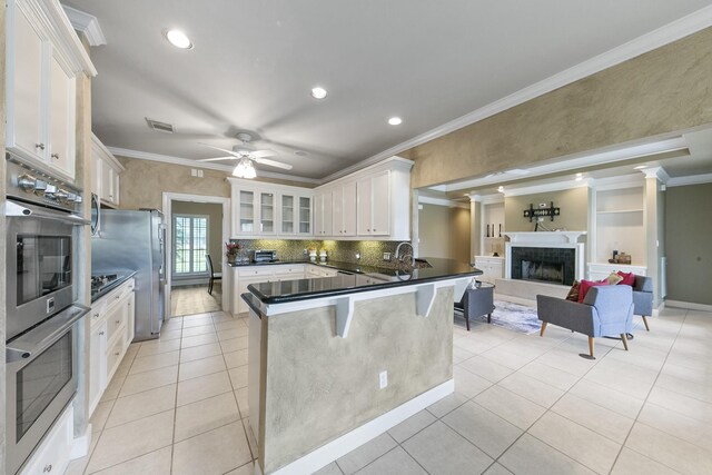 kitchen with a breakfast bar area, appliances with stainless steel finishes, kitchen peninsula, ceiling fan, and white cabinets