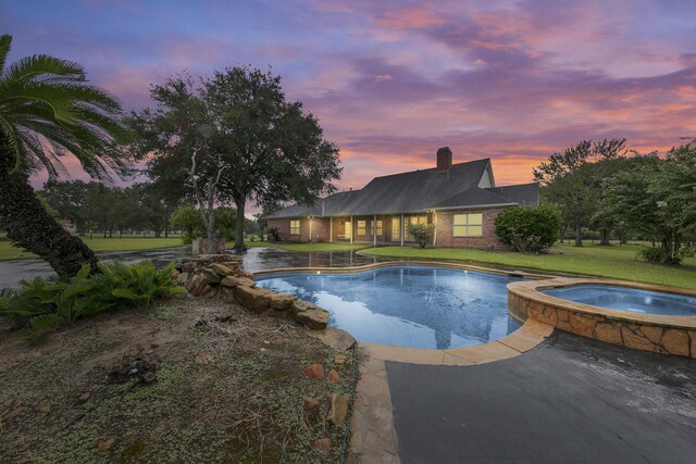 pool at dusk with a yard and an in ground hot tub