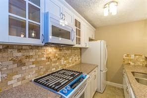 kitchen featuring stainless steel stove, light stone countertops, white cabinetry, tasteful backsplash, and a textured ceiling