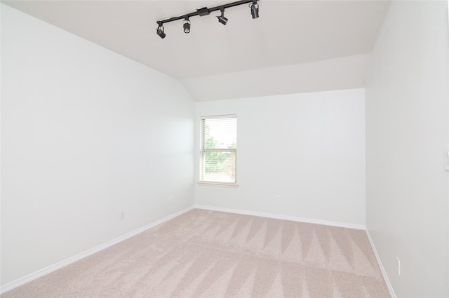 spare room featuring lofted ceiling, rail lighting, and light colored carpet