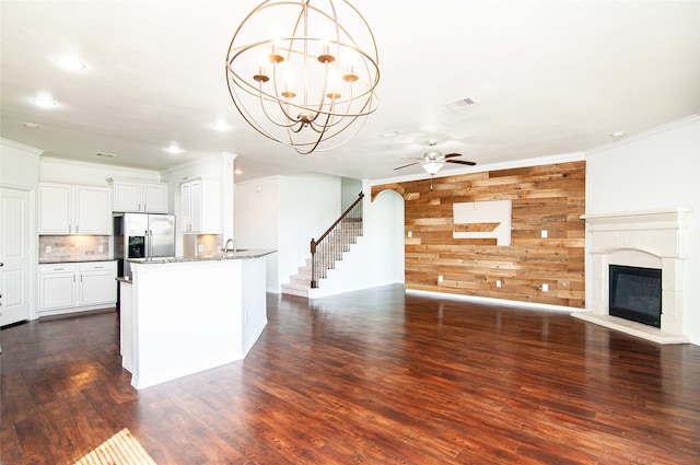 kitchen with wooden walls, crown molding, ceiling fan with notable chandelier, dark hardwood / wood-style floors, and white cabinets