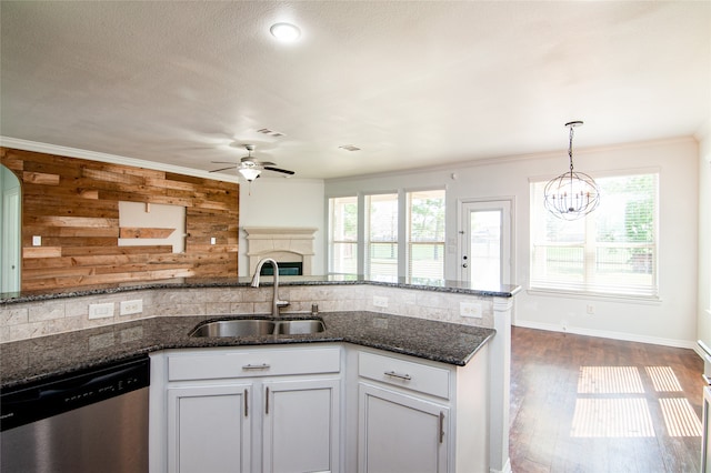 kitchen featuring a wealth of natural light, stainless steel dishwasher, ceiling fan with notable chandelier, and wooden walls