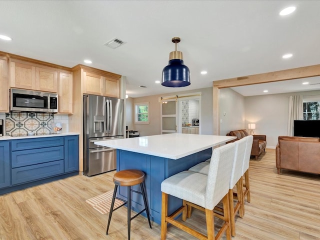 kitchen with backsplash, appliances with stainless steel finishes, hanging light fixtures, and light hardwood / wood-style flooring