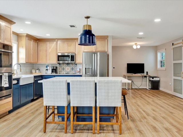 kitchen featuring light hardwood / wood-style floors, light brown cabinets, appliances with stainless steel finishes, and hanging light fixtures