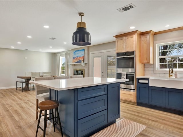 kitchen featuring stainless steel double oven, light wood-type flooring, hanging light fixtures, and a healthy amount of sunlight