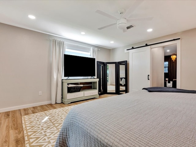 bedroom with a barn door, light wood-type flooring, ceiling fan, and multiple windows