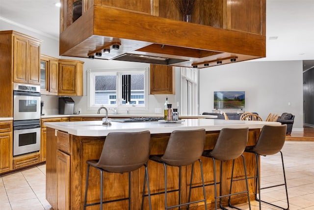 kitchen with a kitchen breakfast bar, an island with sink, stainless steel appliances, ornamental molding, and light tile patterned flooring