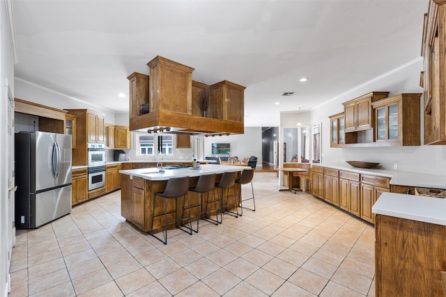 kitchen featuring stainless steel appliances, light tile patterned flooring, a kitchen breakfast bar, a center island with sink, and ornamental molding