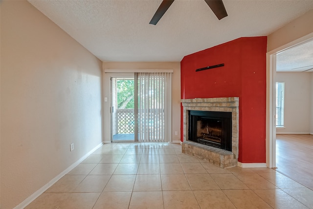 unfurnished living room featuring a brick fireplace, ceiling fan, light tile patterned flooring, and a textured ceiling