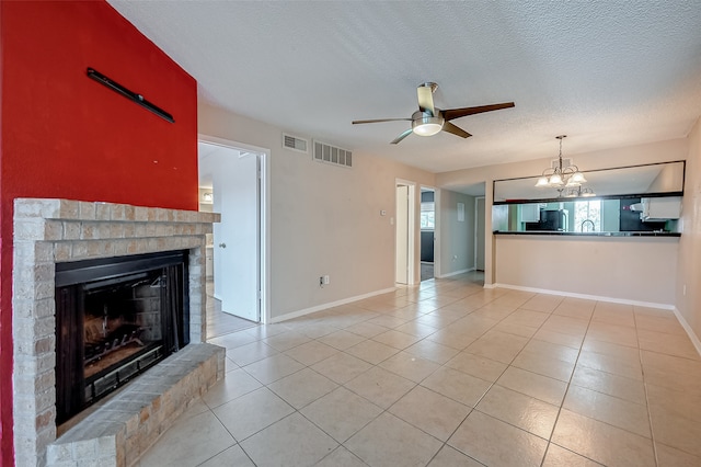 unfurnished living room with light tile patterned flooring, a brick fireplace, ceiling fan with notable chandelier, a textured ceiling, and sink