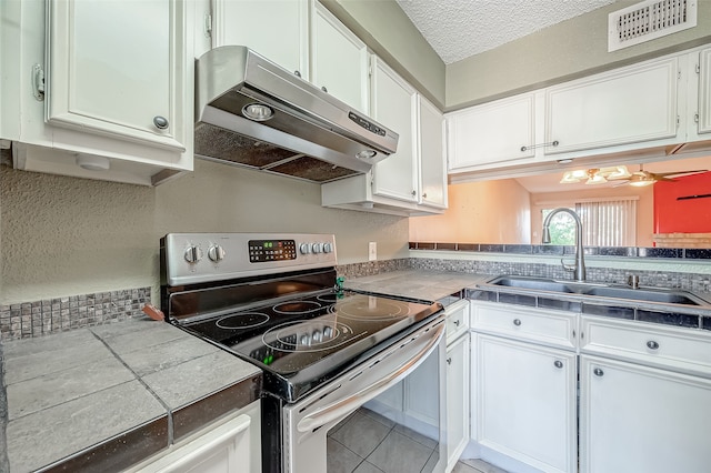 kitchen featuring tile counters, white cabinetry, sink, and stainless steel range with electric cooktop