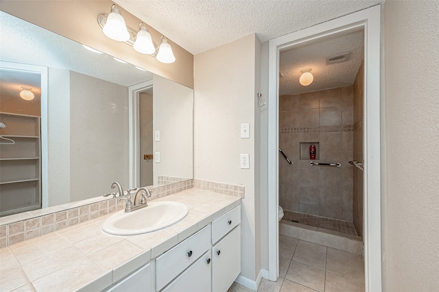 bathroom with vanity, a textured ceiling, a tile shower, tile patterned floors, and toilet