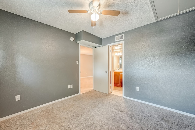 unfurnished bedroom with ceiling fan, connected bathroom, a textured ceiling, and light carpet