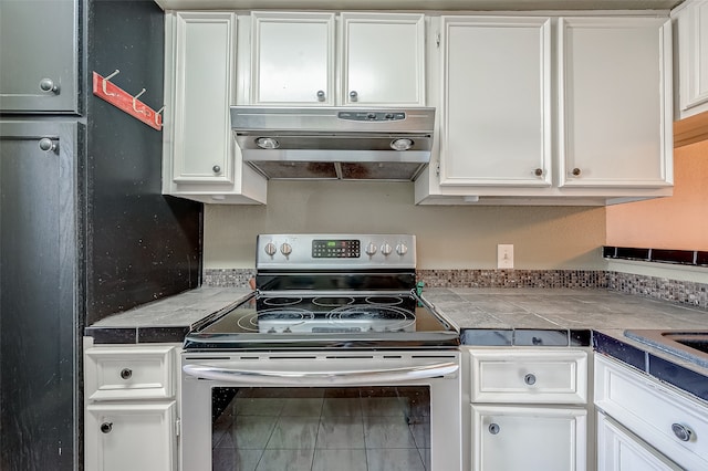 kitchen featuring stainless steel electric range oven, tile counters, range hood, and white cabinets