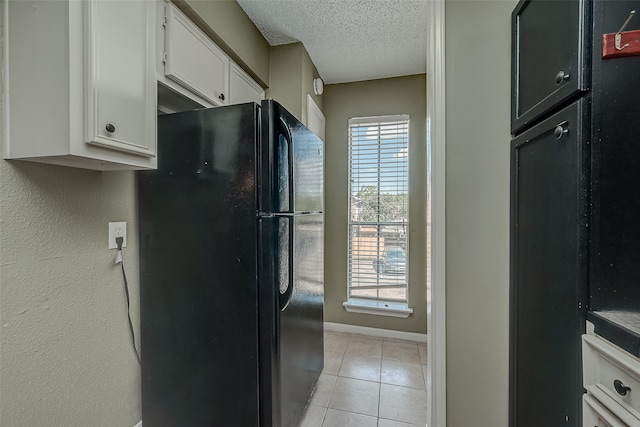 kitchen featuring a textured ceiling, a healthy amount of sunlight, white cabinets, and black refrigerator