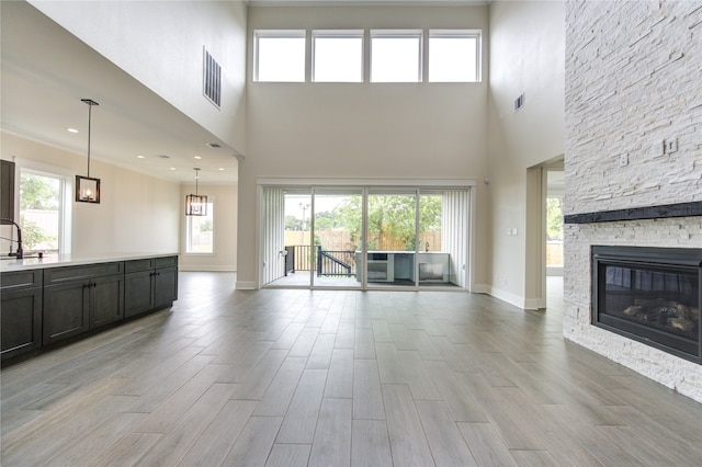 unfurnished living room featuring light wood-type flooring, sink, a towering ceiling, and a stone fireplace