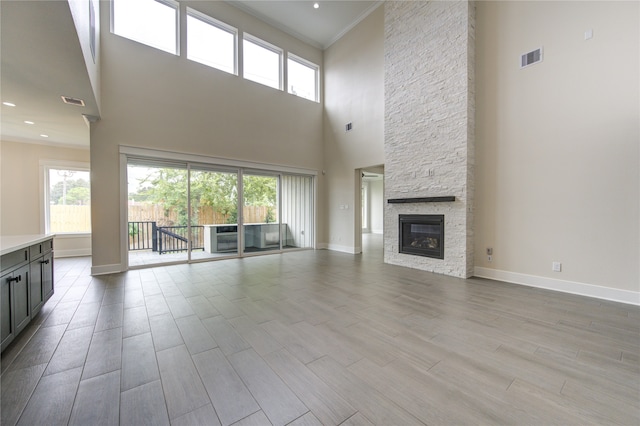 unfurnished living room featuring light wood-type flooring, a fireplace, a towering ceiling, and ornamental molding