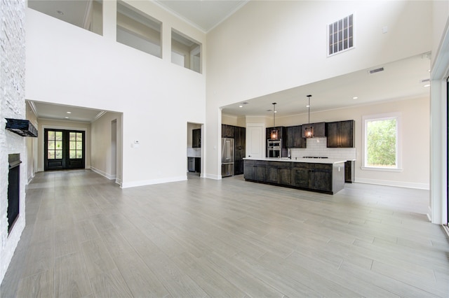 unfurnished living room with a towering ceiling, sink, light hardwood / wood-style floors, and ornamental molding